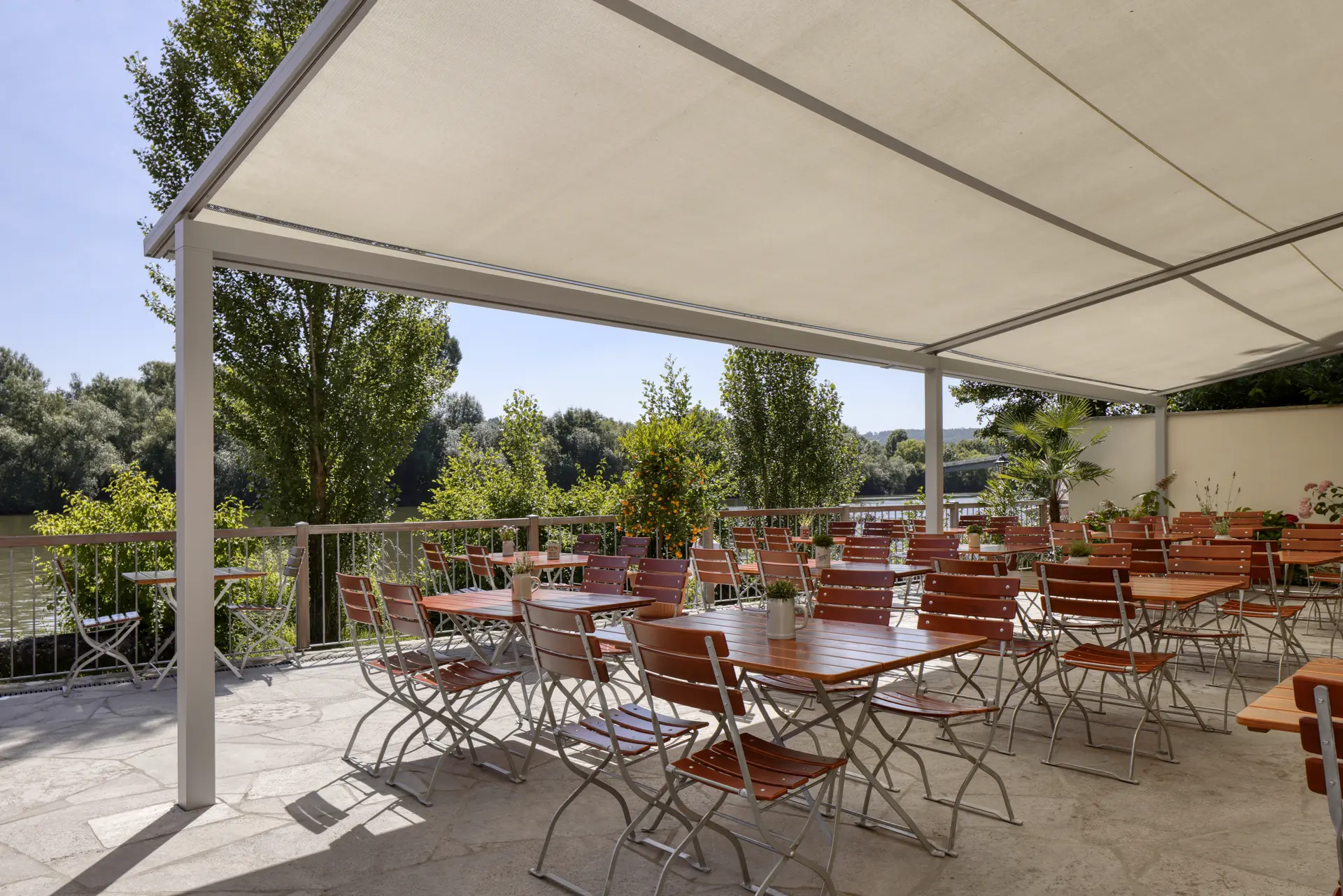 Pergola-Markise über einem Außenbereich eines Restaurants mit mehreren Holzstühlen und Tischen