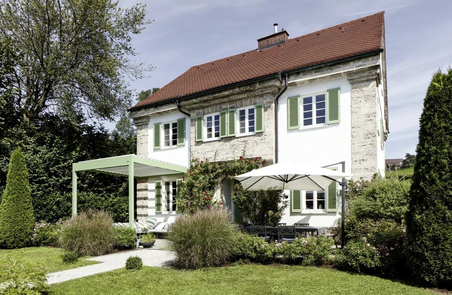 Charmantes Landhaus mit einem grünen Garten und einer Terrasse mit Sonnenschirm
